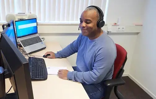 Servicedesk medewerker zit aan bureau met meerdere computerschermen en is aan de telefoon.