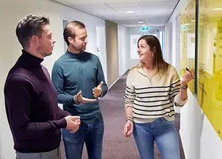 Drie mensen met elkaar in gesprek op de gang voor een whiteboard